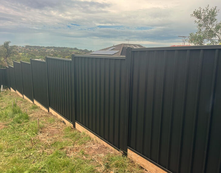 sloped Colorbond fence with reinforced posts and timber sleepers installed in Berwick